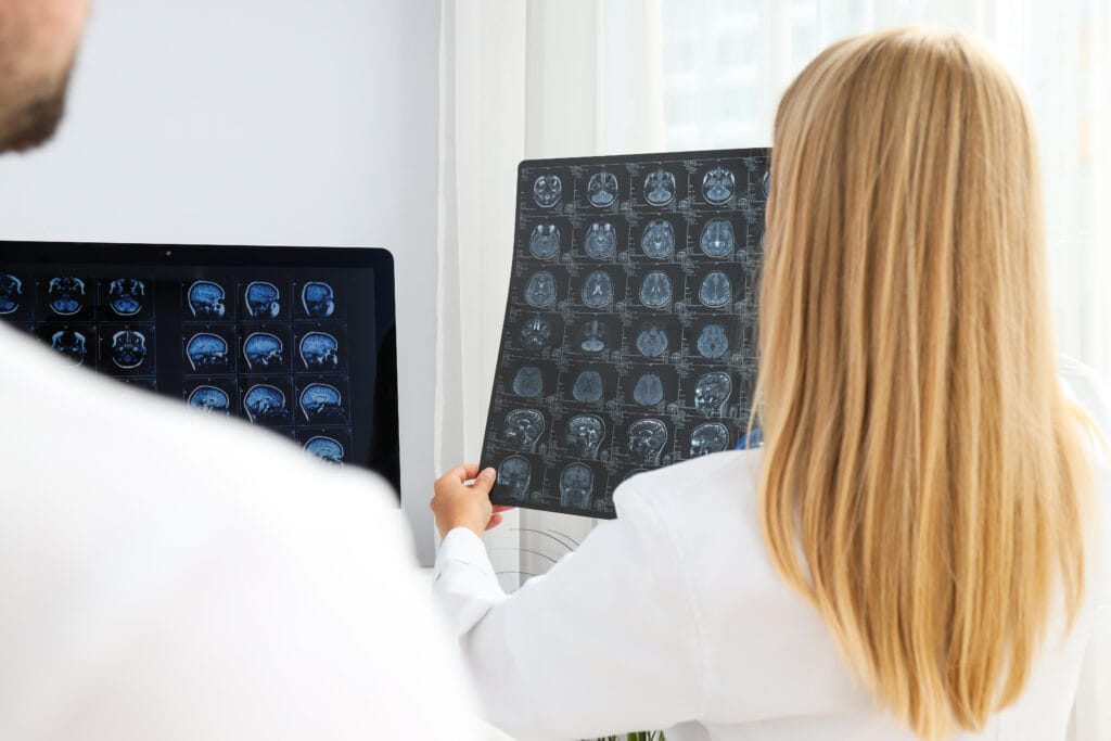Two doctors examine MRI images of a human brain in a medical office.