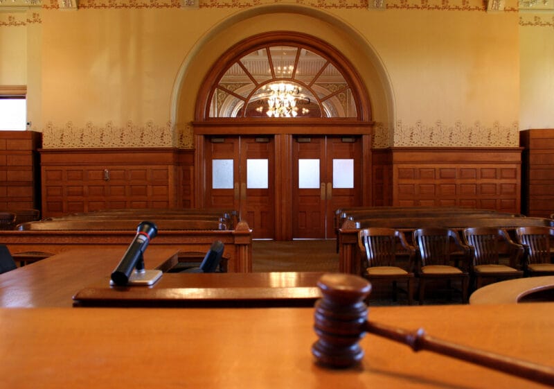 A wooden courtroom interior with empty seats and a gavel on the judge's bench.
