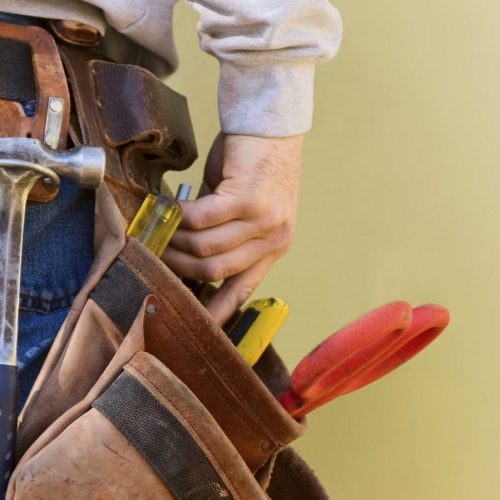 Close-up of a person wearing a tool belt with various tools, including a hammer and pliers.