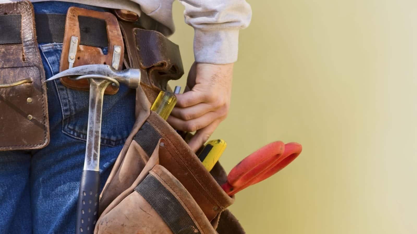 Close-up of a person wearing a tool belt with various tools, including a hammer and pliers.