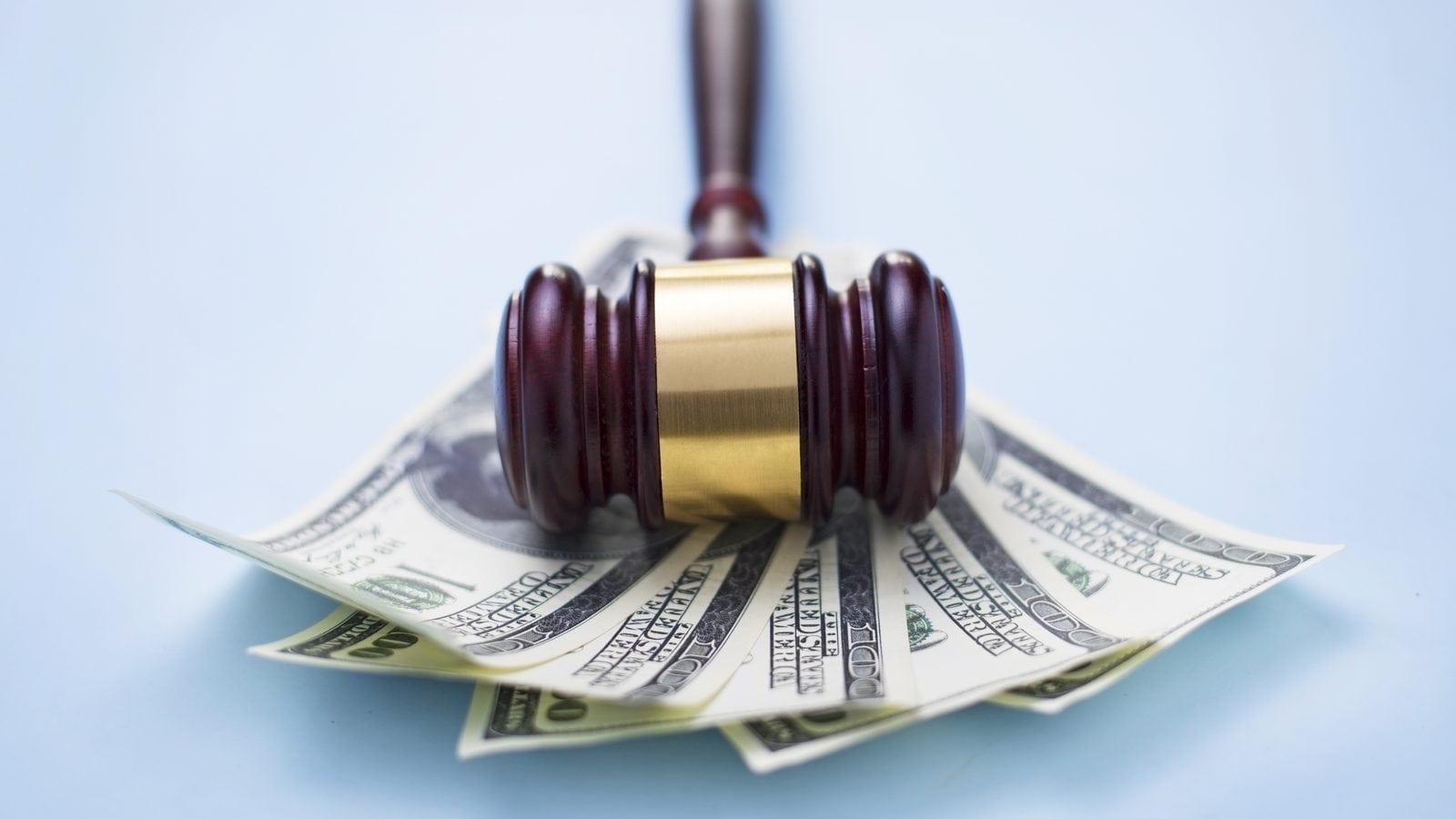 A judge's gavel resting on a pile of hundred-dollar bills.